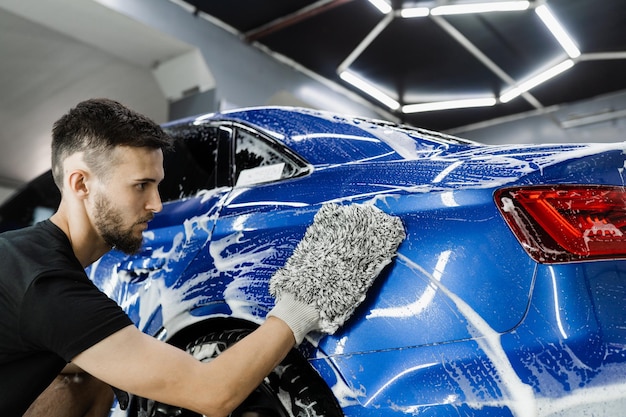 Autowasmachine doet handmatige schuimwas in autodetailservice Handen wassen met microvezelhandschoen met schuimautocarrosserie in garage