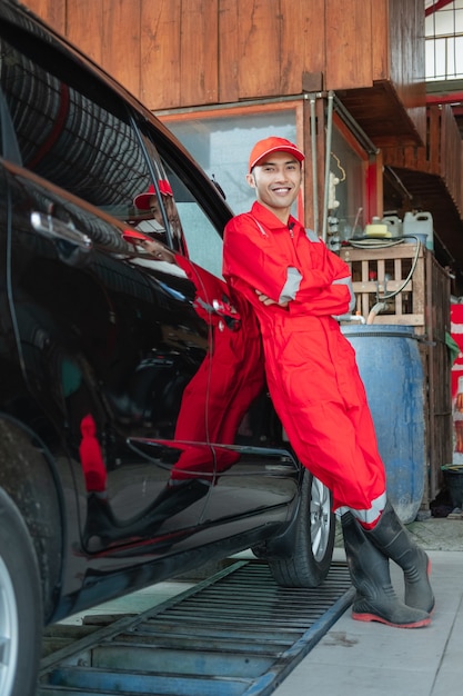 Autowasserette die rode uniforme status draagt die tegen de auto in de wasstraat leunt