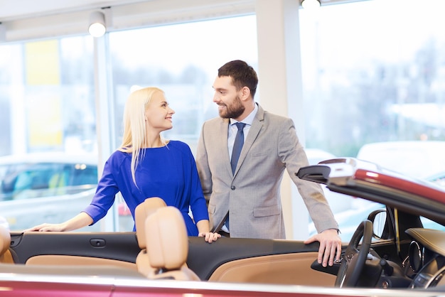 Autozaken, autoverkoop, consumentisme en mensenconcept - gelukkig paar dat auto in autoshow of salon koopt