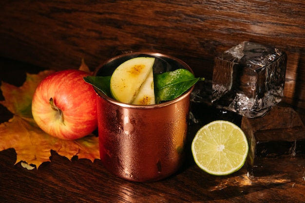 Autumn apple cocktail with ice and lime in iron mug on the table in restaurant