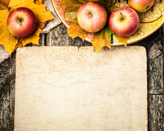 Autumn background from apples and maple leaves on wooden table. Vintage paper blank with copyspace