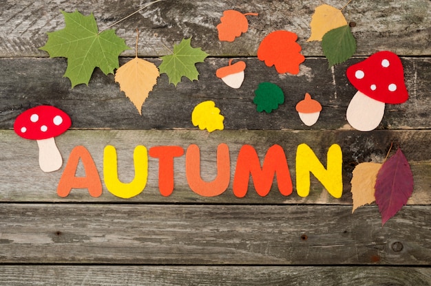 Autumn background on old wooden background. Handmade leaves, mushrooms, acorns and inscription Autumn made of felt