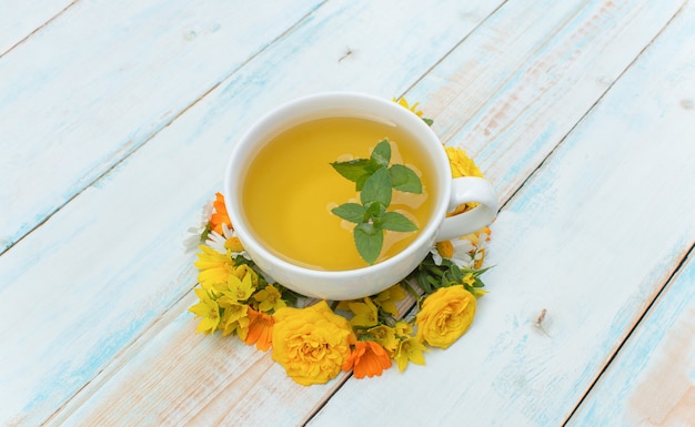 Autumn background. Tea mug with mint and autumn flowers on a wooden background. Concept Autumn Time Fall