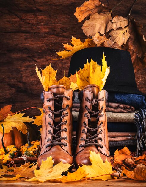 Autumn background with brown leather boots fall warm clothes\
scarves and felt hat pumpkins maple and oak leaves on rustic wood\
background country style female stylish outfit