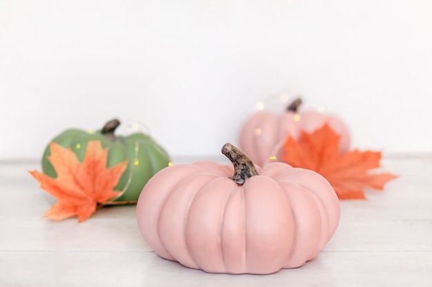 Autumn background with pink and green pumpkins and leaves in pastel shades on light background.
