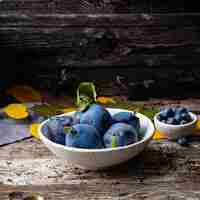 Photo autumn background with ripe violet blue plums in white bowl on old grey wooden table side view