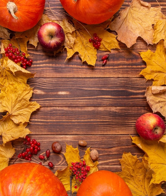 Осенний фон с желтыми кленовыми листьями, тыквами, красными яблоками и ягодами.