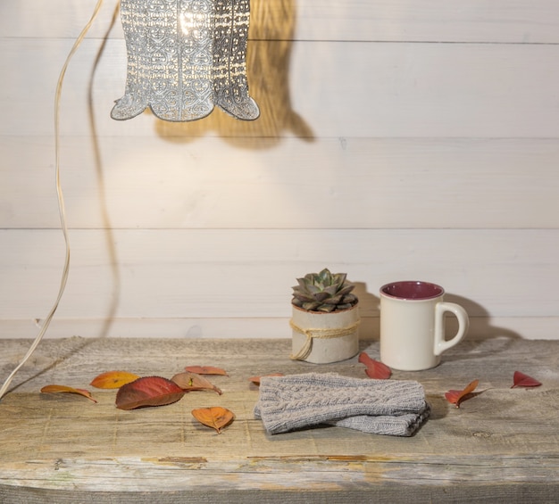 Autumn background, woolen mittens, colorful leaves, succulent, cup of coffee on a vintage wooden table and retro lamp.