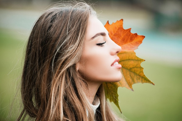 Autumn beauty close up photo of fashion woman with fall maple leaf outdoors