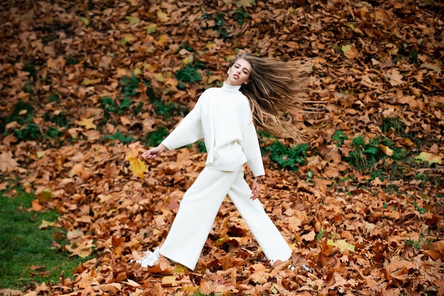 Bellezza autunnale donna moda wodel con foglia d'acero caduta all'aperto a figura intera in movimento moda autunnale