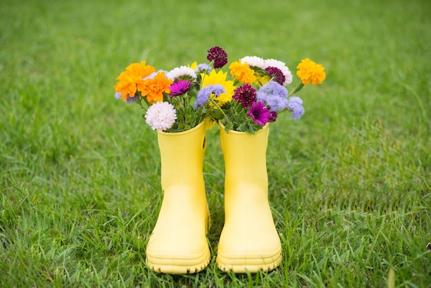 An autumn bouquet of flowers in yellow boots on a background of green grass