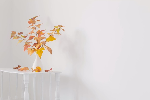 Autumn bouquet in white vase on wooden shelf in white interior