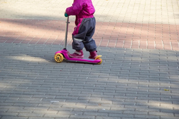 秋に、子供はオーバーオールのタイルの小道に沿ってスクーターに乗ります