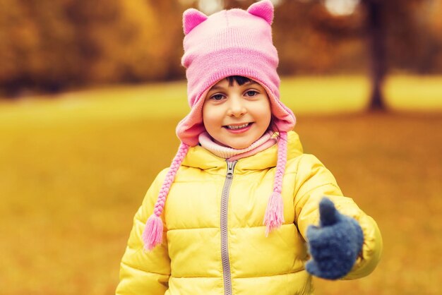 autumn, childhood, happiness, gesture and people concept - happy beautiful little girl showing thumbs up outdoors