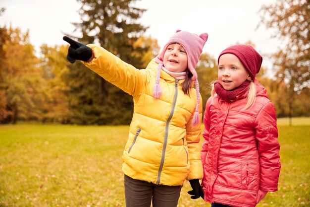 autumn, childhood, leisure, gesture and people concept - happy little girls pointing finger in park outdoors