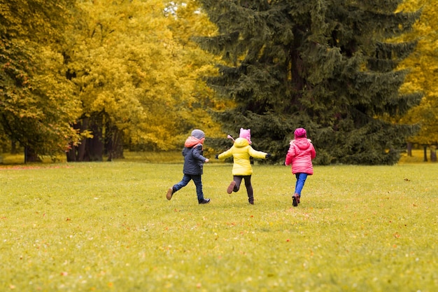 autumn, childhood, leisure and people concept - group of happy little kids playing tag game and running in park outdoors