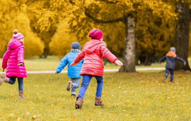 autumn, childhood, leisure and people concept - group of happy little kids playing tag game and running in park outdoors