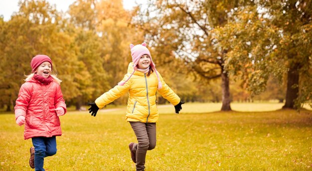 autumn, childhood, leisure and people concept - happy little girls playing tag game and running in park outdoors