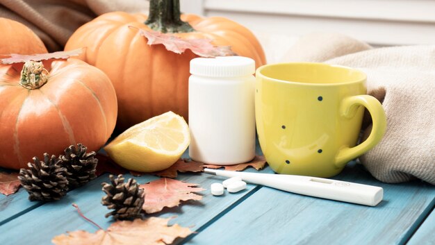 Осенняя простуда, чай с лимоном, градусником, имбирем, тыквой, таблетками и сухими листьями на черном фоне. вид сверху, плоская планировка