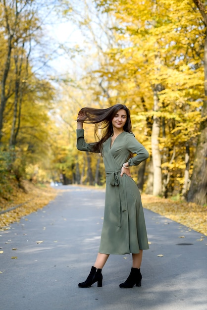 Осенние краски. Красивая женщина в пальто позирует в лесу на обочине дороги