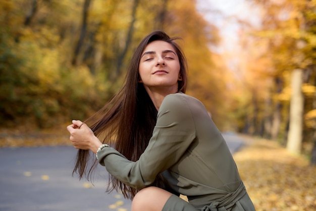 Colori autunnali. bella donna in cappotto in posa nella foresta sul ciglio della strada