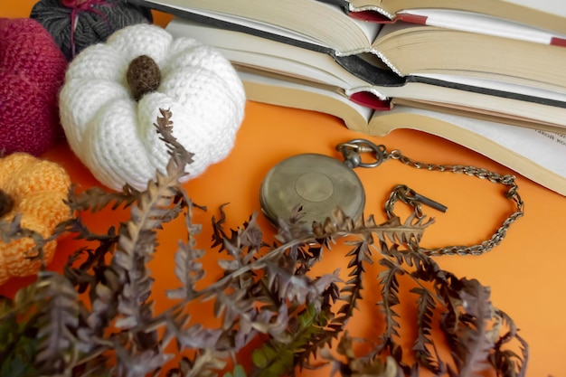 秋の組成物カボチャの隣のオレンジ色の背景に本、植物標本、アンティーク時計 時間と本