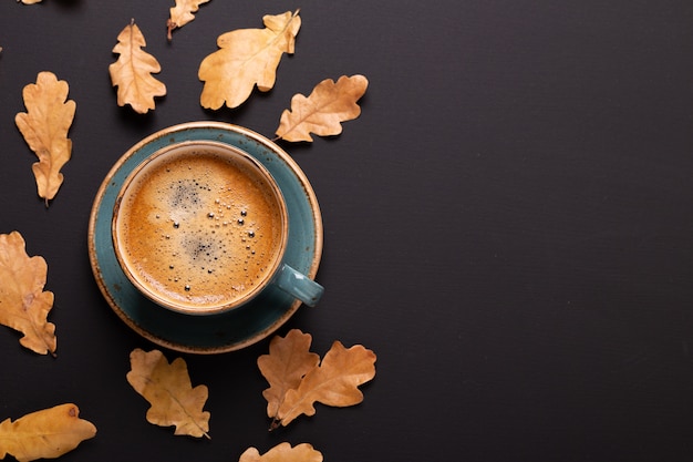 Autumn composition. Cup of coffee and dry leaves on black background.