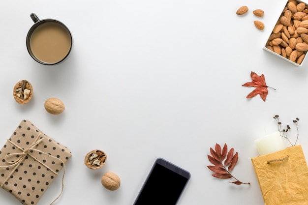 Autumn composition. Cup of coffee, sartphone, dried leaves on white