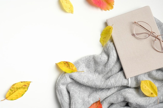 Autumn composition Knitted sweater yellow leaves paper notebook and glasses on white background