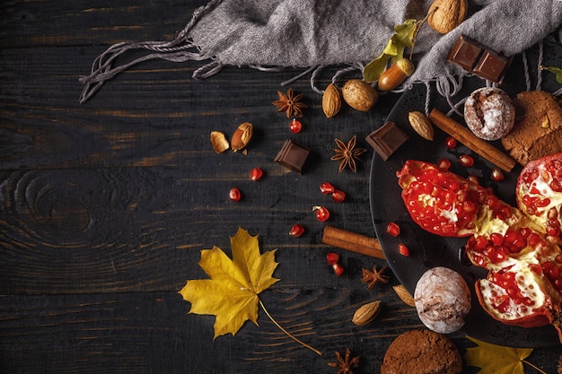 Autumn composition. Pomegranate with nuts, spices and dry leaves on a dark wooden table. Top view.