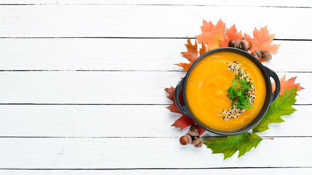 Autumn composition Pumpkin soup with pumpkin and colored autumn leaves flat lay On a white wooden background Top view Free space for your text