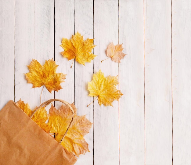 Autumn composition shopping paper bag autumn maple leaves on a wooden white background Top view copy space