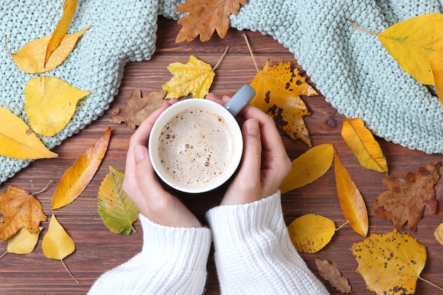 Autumn composition top view cup of coffee in the hands and autumn leaves