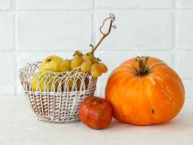 Autumn composition with a big pumpkin and fruits. Pumpkin and wicker basket with an apple, a pear and grape on a white background. Free space for text. Autumn shopping. Thanksgiving Day.