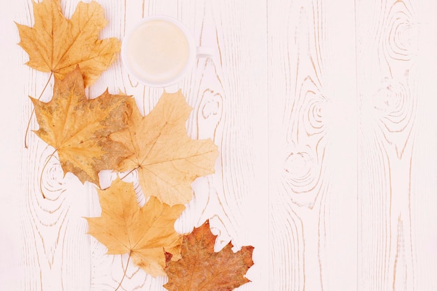 Autumn composition with a cup of coffee autumn yellow dry maple leaves on a rustic whitewashed wooden background Flat lay copy space