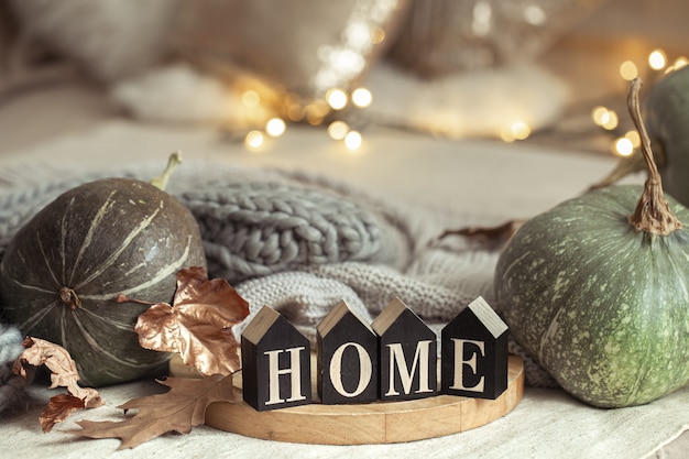 Autumn composition with pumpkins and wooden letters with the words home on blurred background with bokeh.