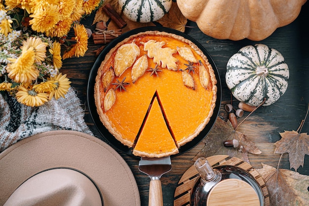 フレームの中央にカボチャの黄茶の花の暖かい格子縞と帽子とカボチャのパイと秋の構成