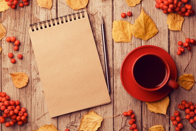 Photo autumn composition with workspace with blank craft notebook, pencil, red cup of coffee and beautiful red maple leaves. top view, flat lay, vintage toning. autumn relax concept