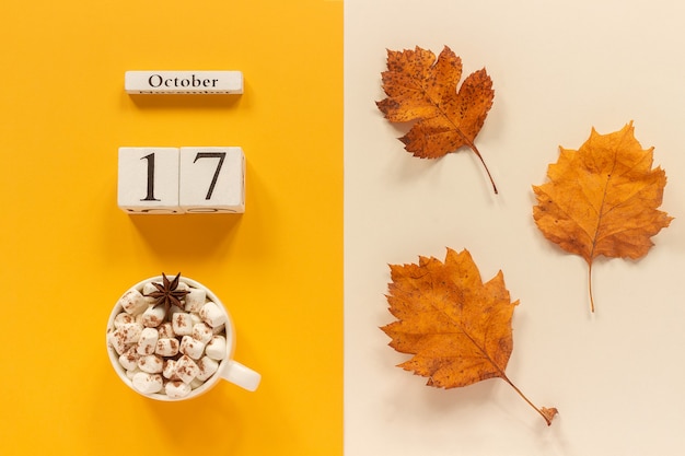 Composizione autunnale. calendario in legno 17 ottobre, tazza di cacao con marshmallow e foglie autunnali gialle su fondo beige giallo. vista dall'alto flat lay mockup concept ciao settembre.