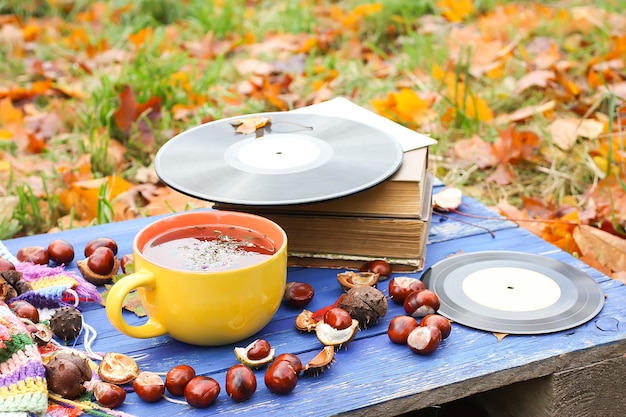 Autumn composition of yellow ceramic cup of herbal tea and vintage vinyl records on aged wooden background with bright handmade crocheted plaid, old book, fall autumn leaves and chestnuts.