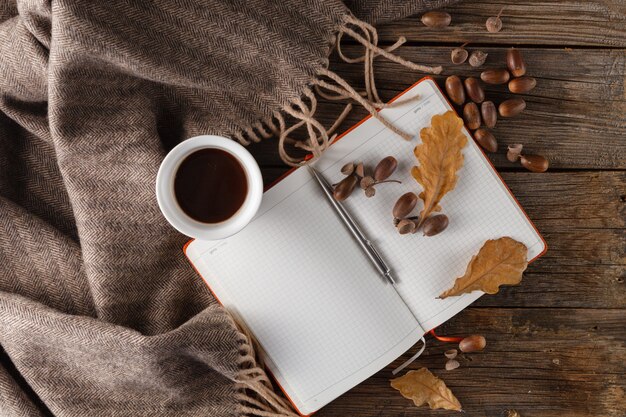 秋のコンセプト、色鮮やかな葉、ドングリ、一杯のコーヒーと木製のテーブル、トップビューでニットスカーフ
