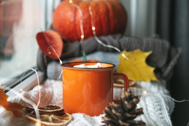 Autumn cozy composition. Cup of cocoa, pumpkin, autumn leaves and a knitted blanket on the windowsill. Autumn, hygge home mood.  Selective focus.