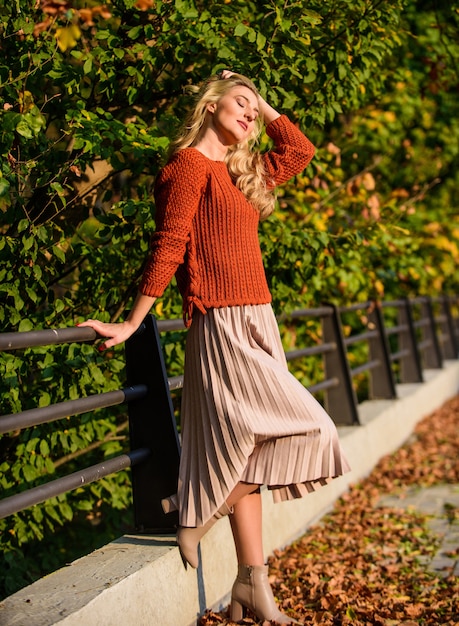 秋の日。屋外の秋の女性。落ち葉のある晴れた日。秋のファッションシーズン。女性の美しさ。女性らしさと優しさ。段ボールのスカートとセーターの女の子。プリーツトレンド。女の子は公園を散歩します。