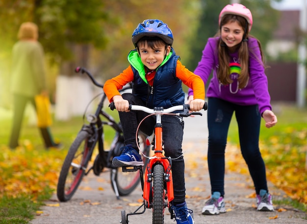 Autumn day. Sister teaches her little brother to ride a bike and rejoices at his success. Family and healthy lifestyle. 