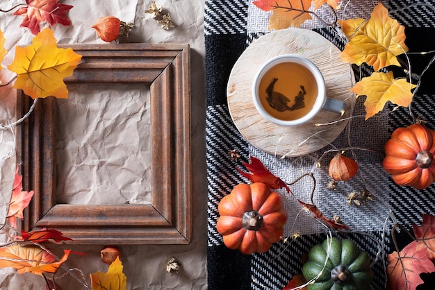 Autumn decor pumpkin with a cup of tea on a plaid plaid wooden frame copy space flat lay