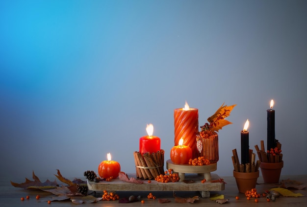 autumn decor with burning candles on wooden shelf on blue background