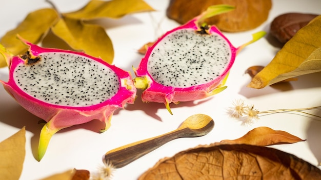 Foto pitahaya di frutta del drago autunno con buccia rossa e polpa bianca su fondo bianco con foglie secche