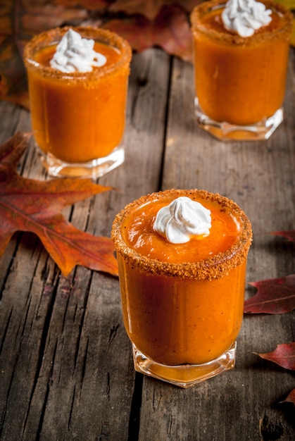Autumn drink. Ideas and recipes for Thanksgivings, Halloween. Alcohol cocktail Pumpkin Pie Vodka Shots on old rustic wooden table with fall leaves, copy space