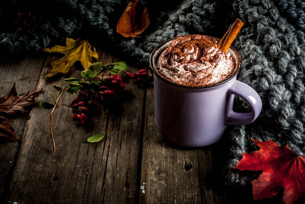 Photo autumn drinks, hot chocolate or cocoa with whipped cream and spices (cinnamon, anise), on the old rustic wooden table, with a warm cozy blanket, hay berry and leaves copyspace