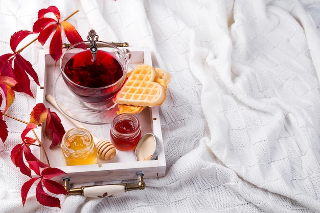 Autumn fall concept with knitted blanket and hot tea with waffer, jam, honey